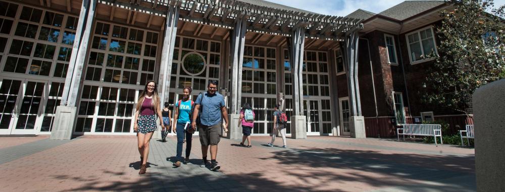Students walking toward a large modern campus building with glass columns under blue sky
