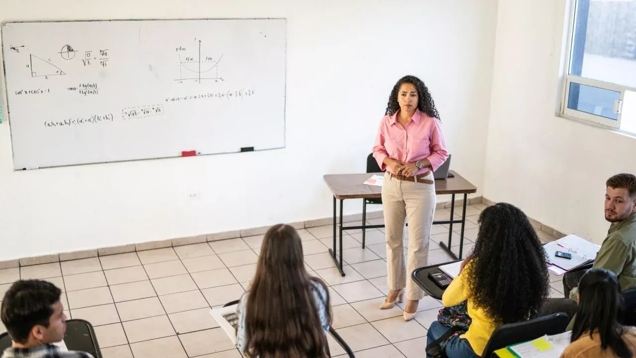 Instructor faces a classroom with a whiteboard in background