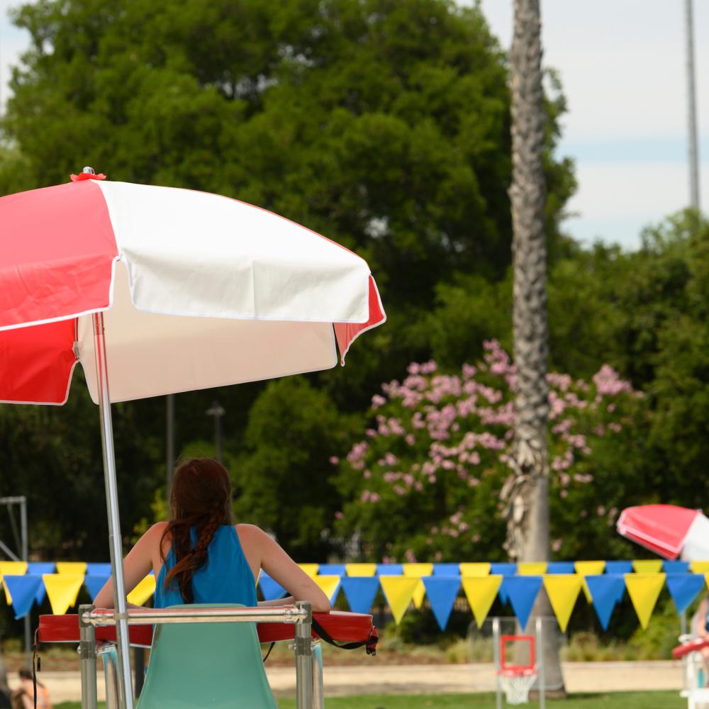 A lifeguard watches over the pool, sitting under a sun umbrella.
