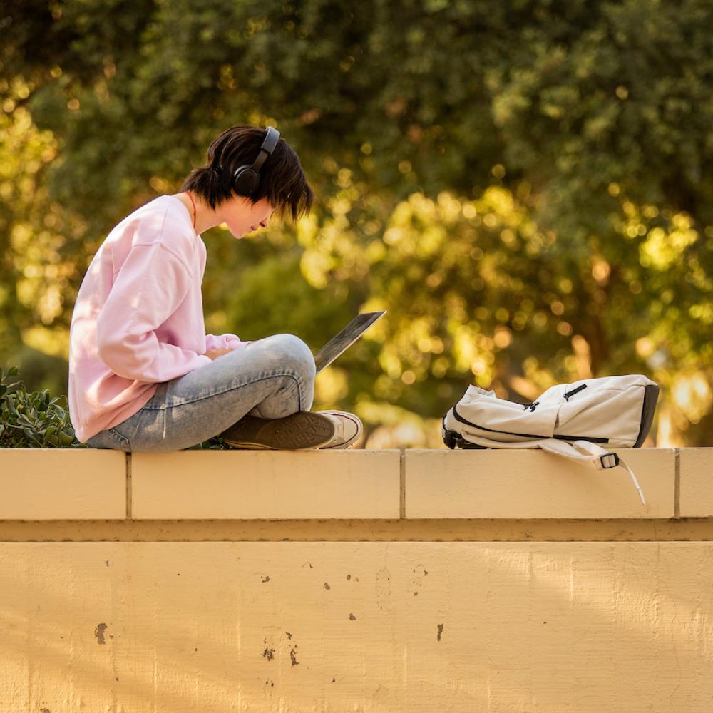 Student with laptop sitting on an outdoor wall.