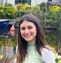 Smiling young woman in light green top by a canal with daffodils and a moored boat