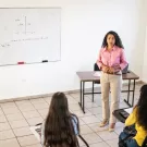 Instructor faces a classroom with a whiteboard in background