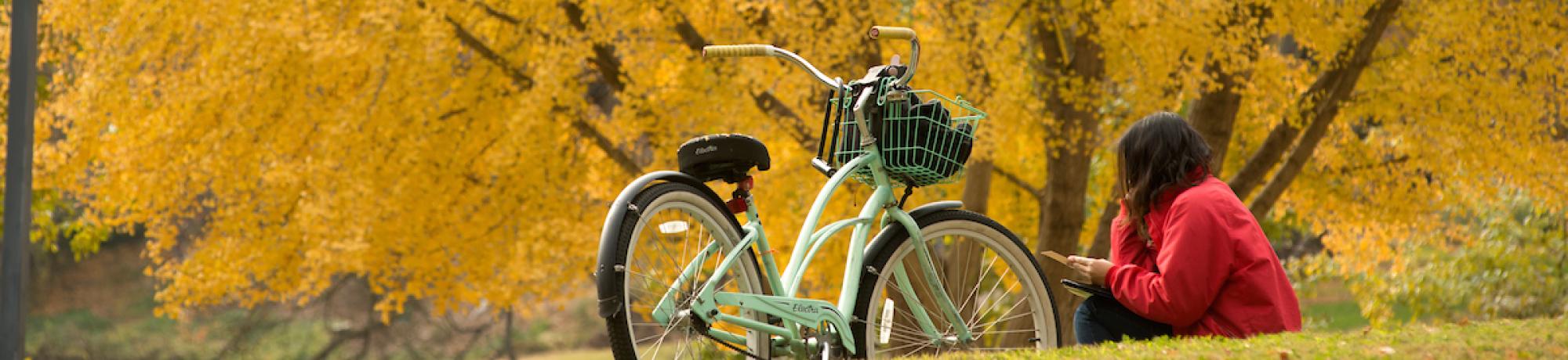 Student studying outside near bike and fall foliage