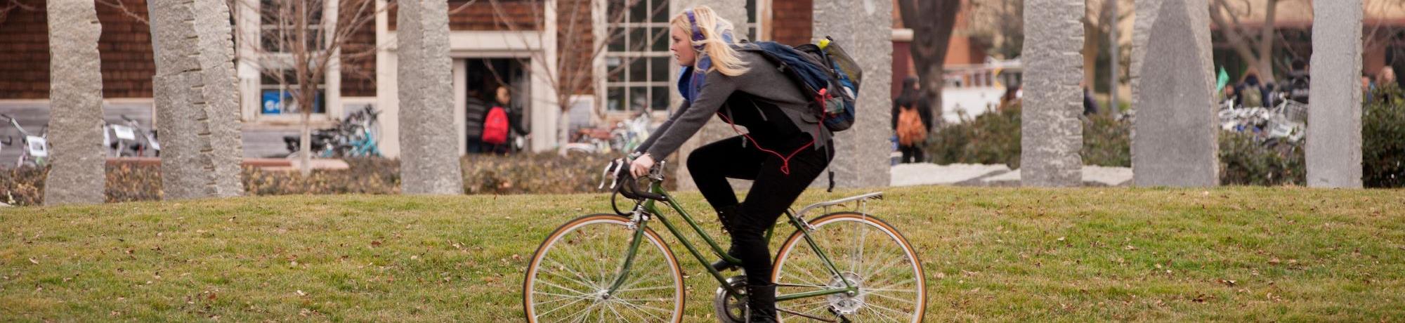 Student riding bike past sculptures