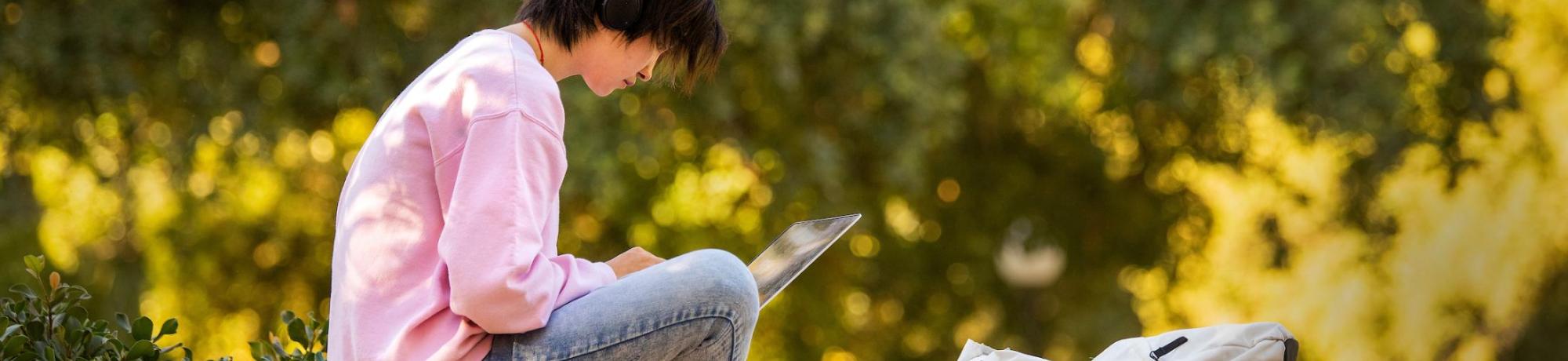 Student with laptop sitting on an outdoor wall.
